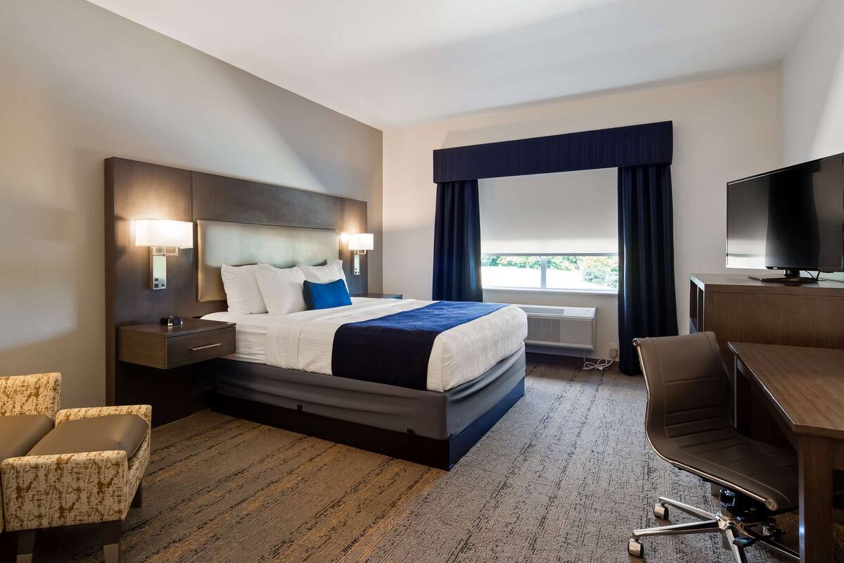 A hotel room with a bed, bedside tables, a desk, a chair, and a television.