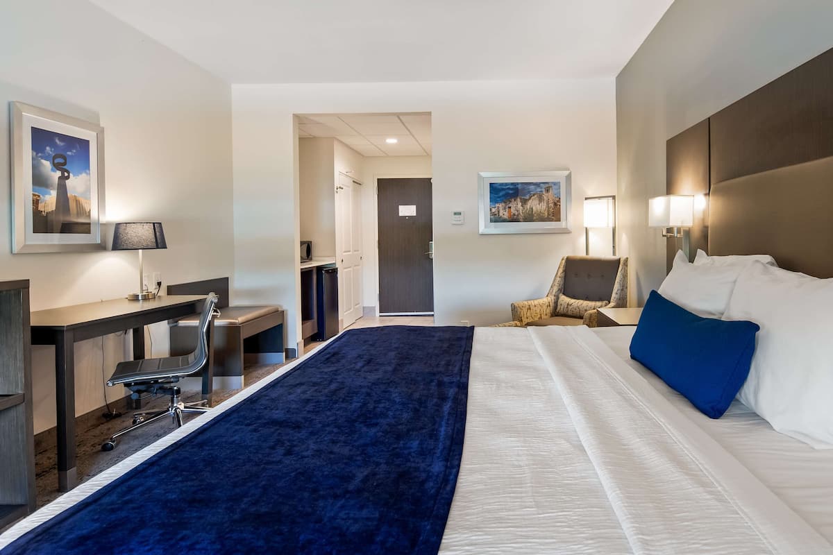 A hotel room with a bed, a desk, a chair, a TV, and a door leading to a hallway.