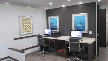 A modern office space with two desks, each with a computer monitor, black office chairs, and a framed picture on the wall.