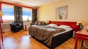 A hotel room with a large bed, a small table, a chair, and a window with curtains. - Skoogs BnB (Pitea)