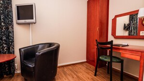 A room with a wooden floor, a black leather chair, a desk with a mirror, and a television mounted on the wall. - Skoogs BnB (Pitea)