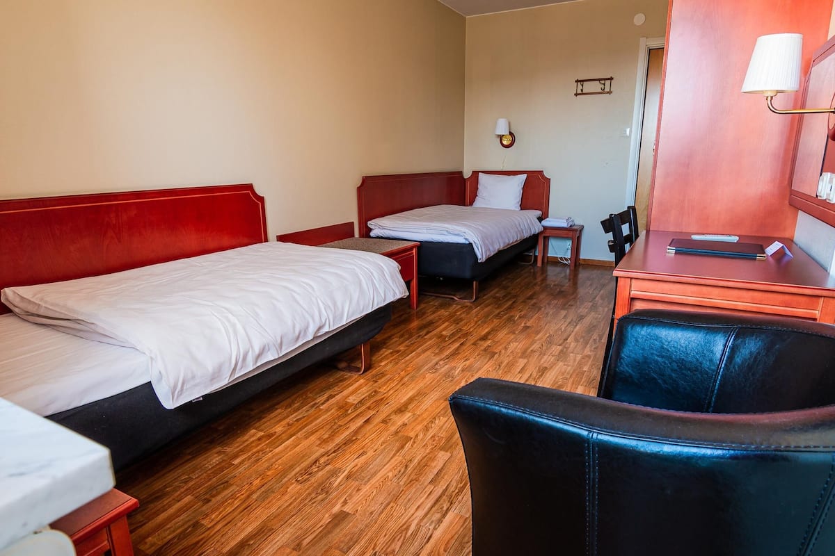 Een hotelkamer met twee enkele bedden, een bureau met stoel, en een bijzettafeltje met lamp.