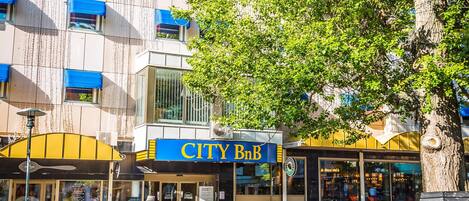Un edificio urbano con un letrero que dice 'CITY B&B', asientos al aire libre y un árbol grande en la parte delantera.