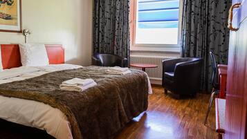 A hotel room with a bed, a chair, a small table, and a window with curtains.