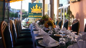 Cenário de restaurante com mesa posta para refeição, cadeiras e uma placa com 'Regat Hotel-restaurant'.