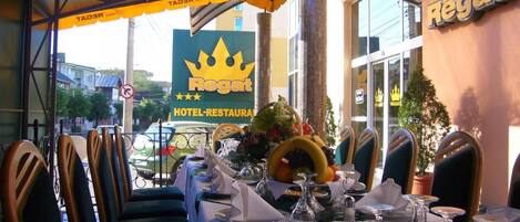 Un restaurante con una mesa dispuesta para comer, sillas y un cartel que dice 'Regat Hotel-restaurant'.
