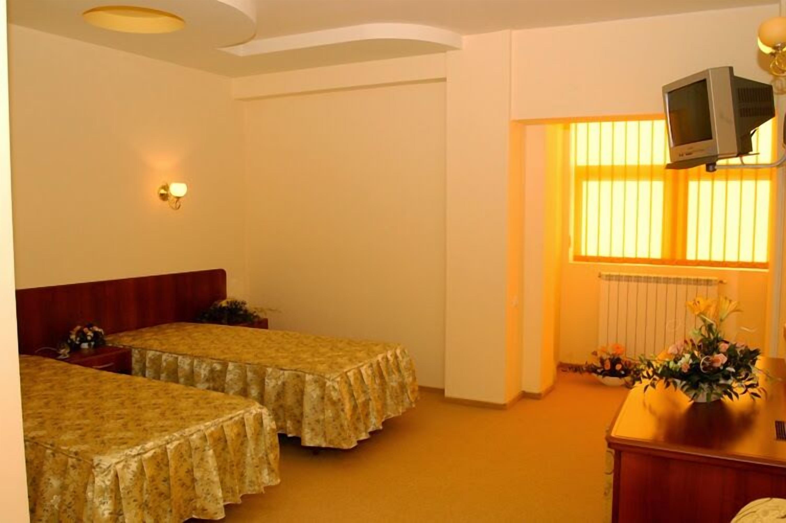 A room with two single beds, a wooden desk, a television on a stand, and a radiator.