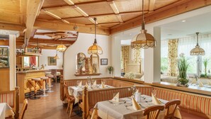 A restaurant with wooden interiors, multiple dining tables, and hanging pendant lights. - Panoramahotel Gürtl (Haus)