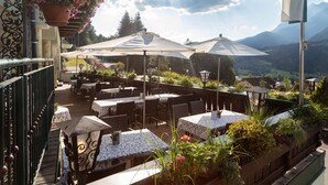 An outdoor patio with tables and chairs, surrounded by potted plants and umbrellas, overlooking a mountainous landscape. - Panoramahotel Gürtl (Haus)