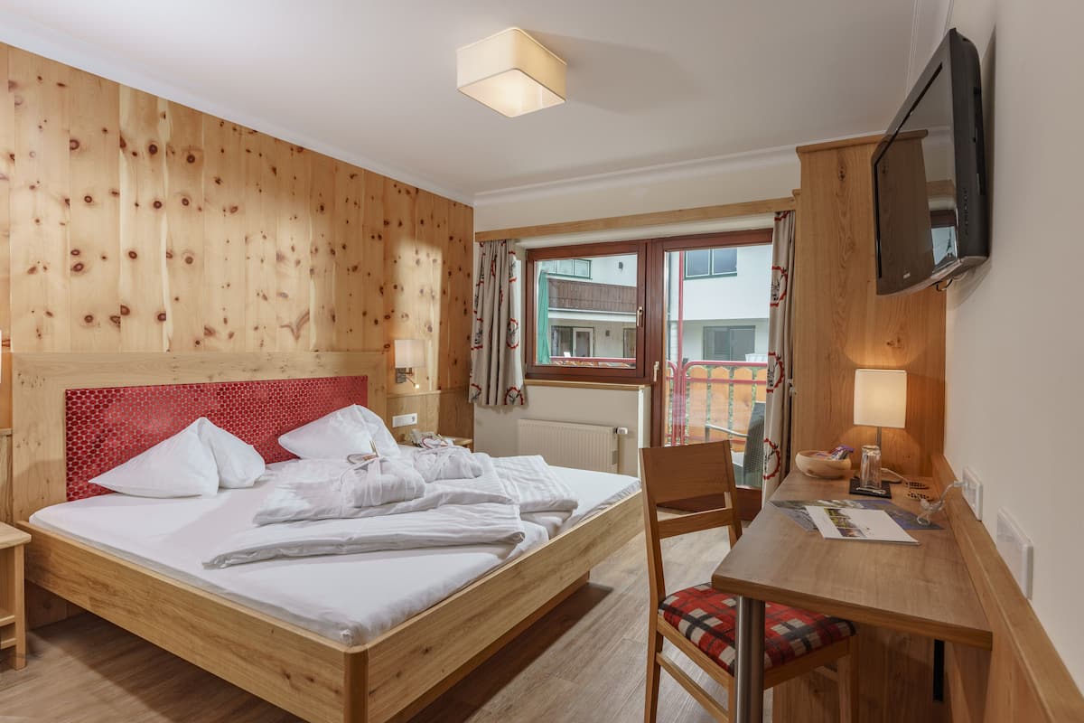 A wooden-paneled room with a bed, a desk, a chair, a TV, and a window with curtains.