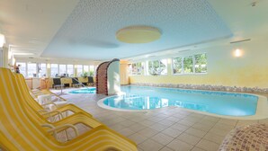 An indoor swimming pool with yellow striped lounge chairs, a brick pillar, and large windows. - Panoramahotel Gürtl (Haus)