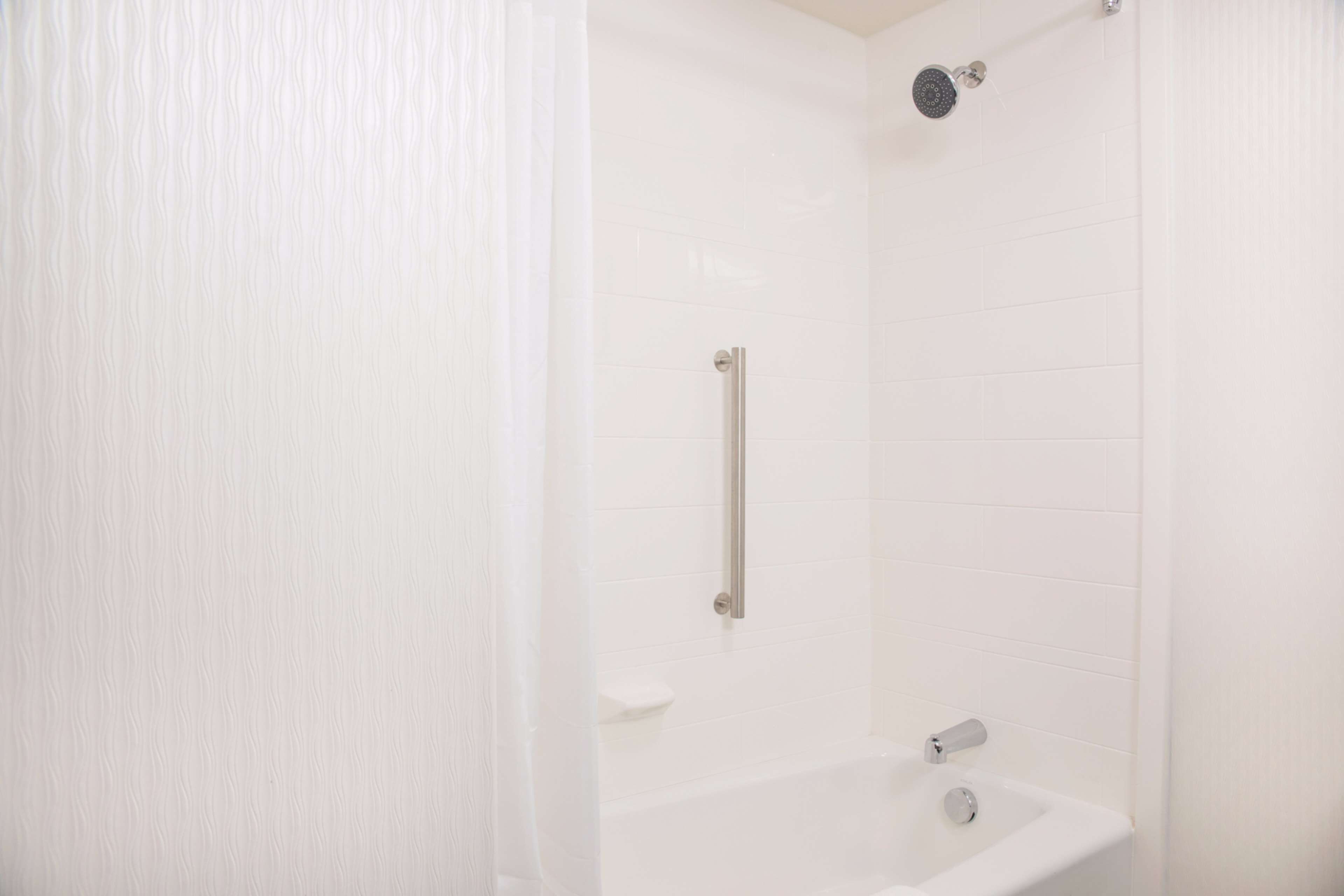 A white bathroom with a shower, a handrail, and a sink.