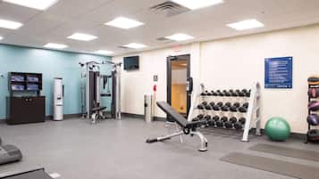Un gimnasio con equipo de ejercicio, un dispensador de agua y un televisor montado en la pared.