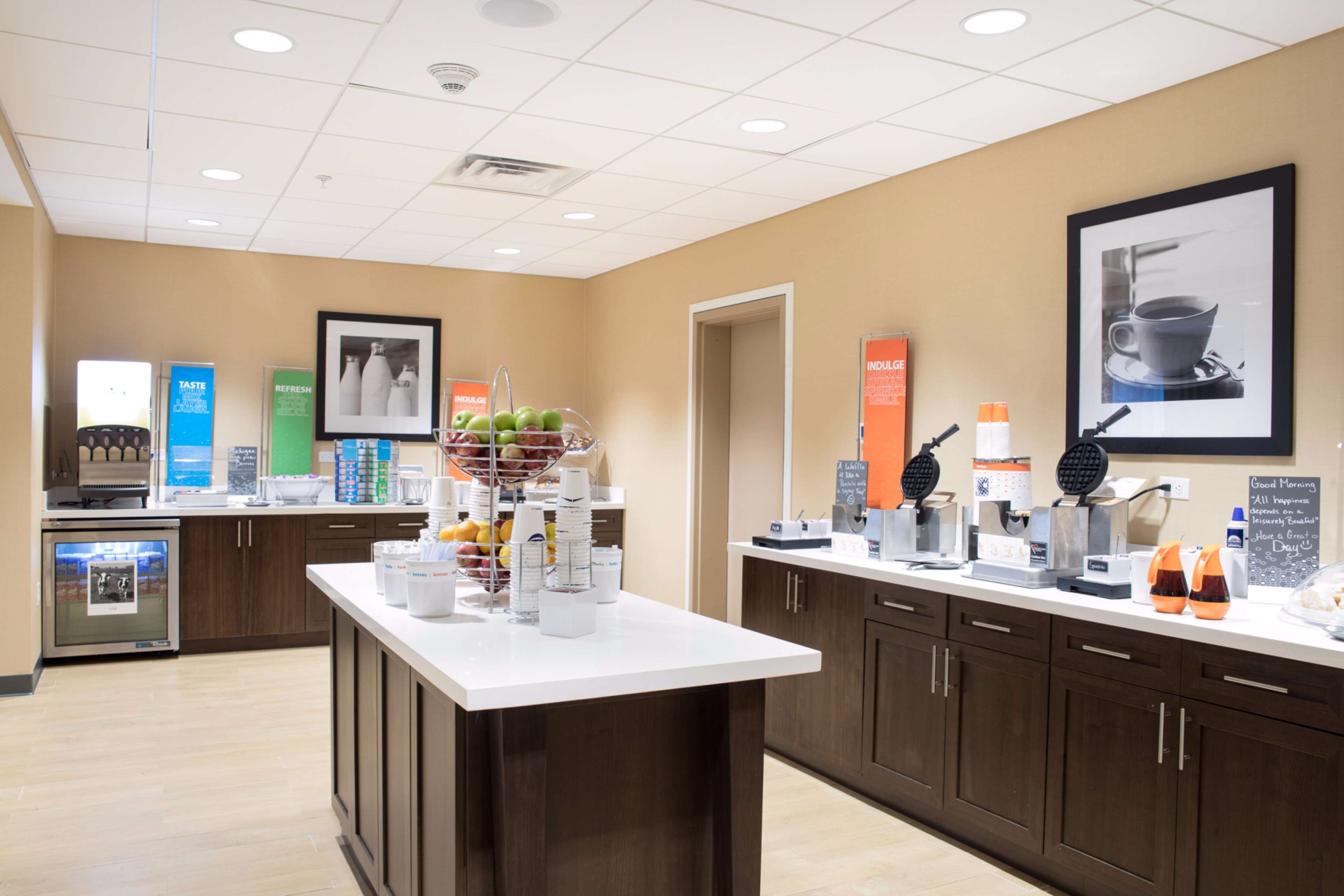 A modern kitchen area with a white countertop, various appliances, and a display of fresh fruits.