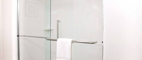 A glass-enclosed shower with a white towel on a metal towel bar.