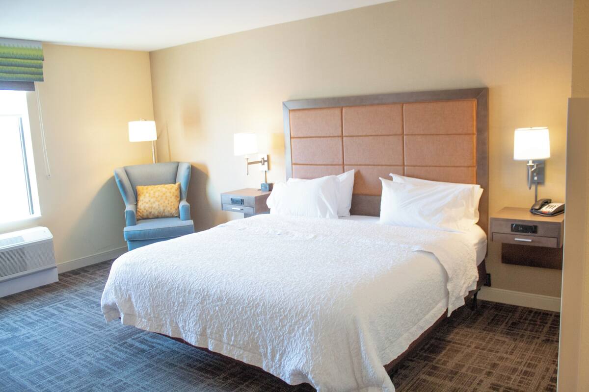 Una habitación de hotel con una cama grande, una silla, una mesita de noche y una lámpara.