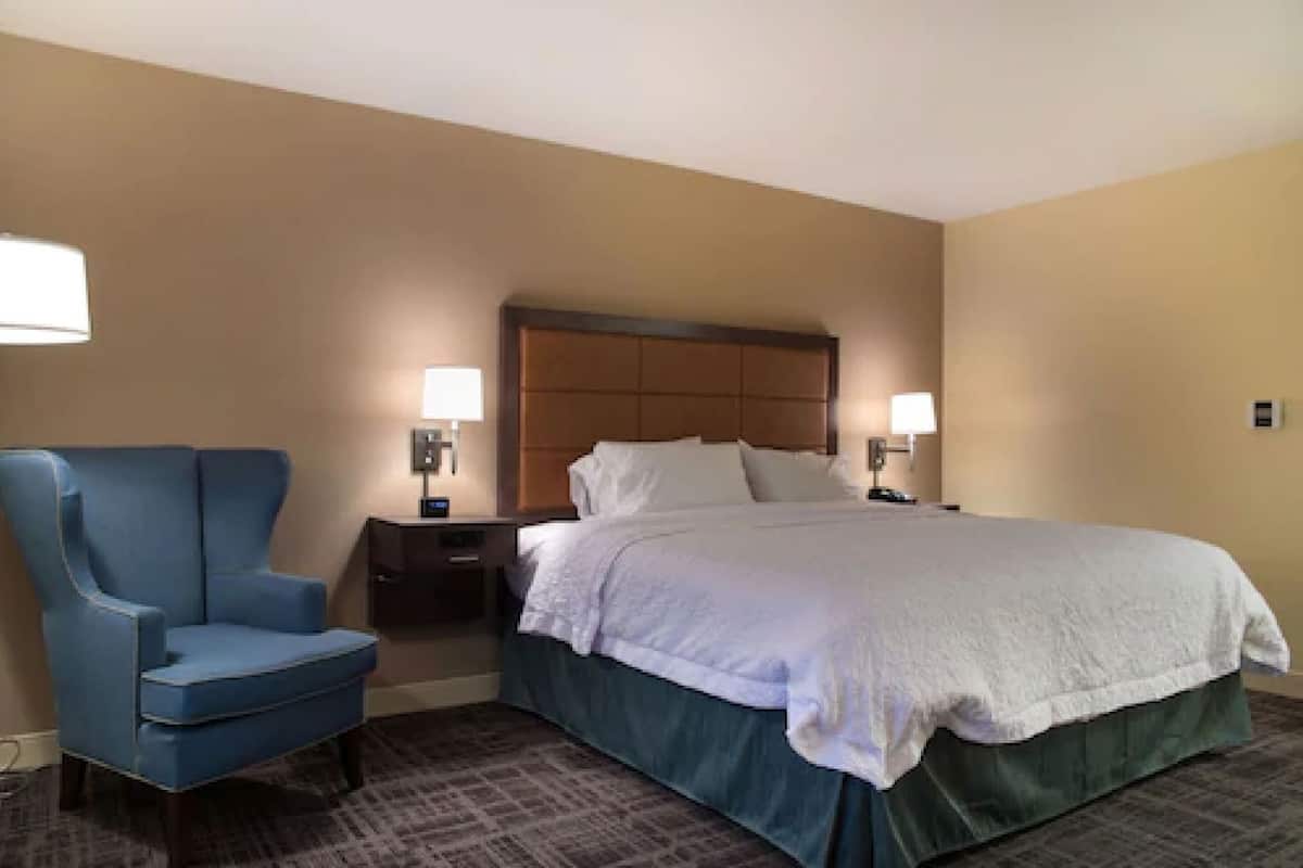 A hotel room with a bed, a chair, a nightstand, and two wall-mounted lamps.
