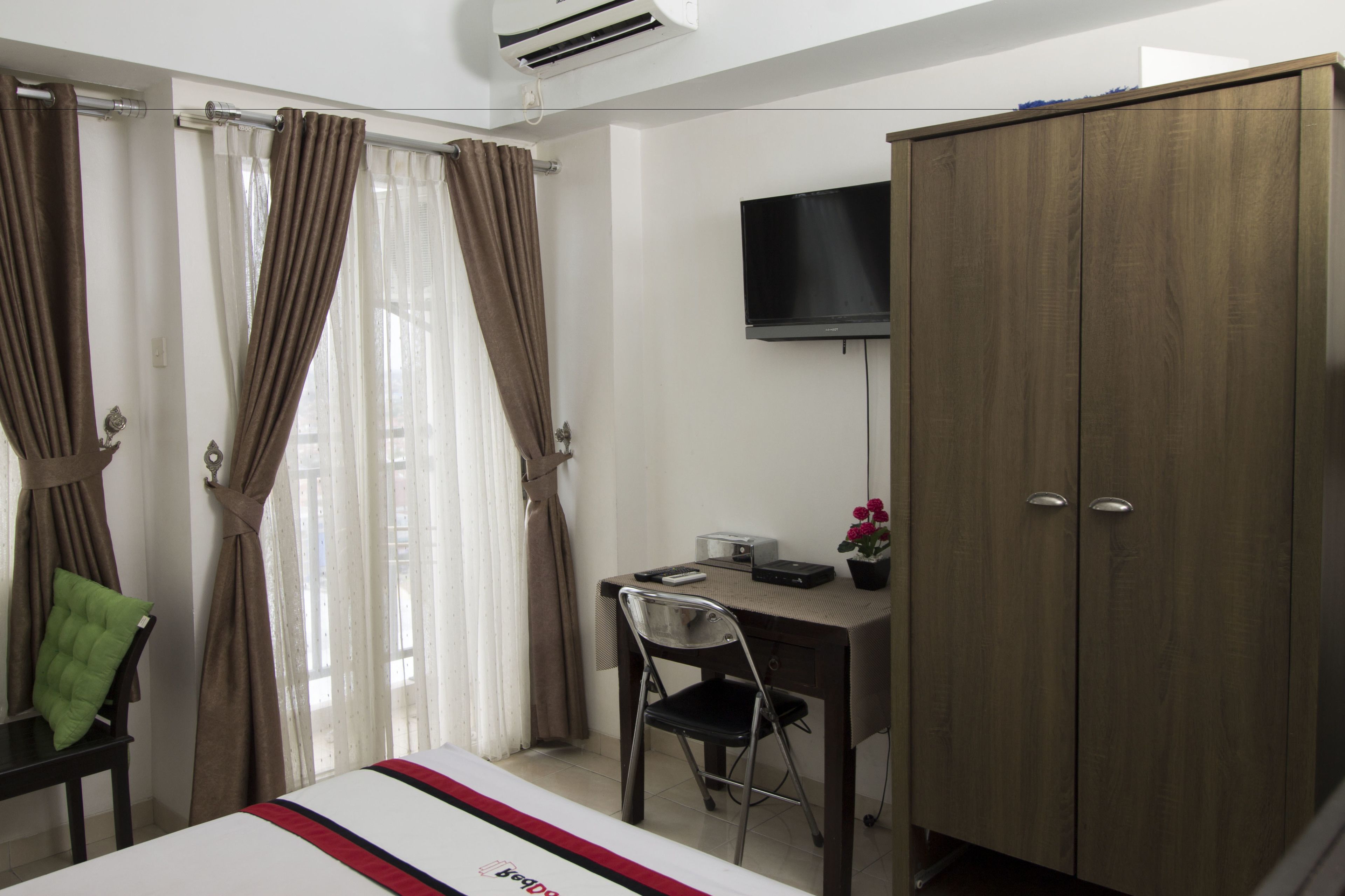 A hotel room with a bed, a desk with a chair, a wardrobe, a television, and curtains.