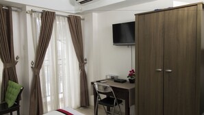 A hotel room with a bed, a desk with a chair, a wardrobe, a television, and curtains.