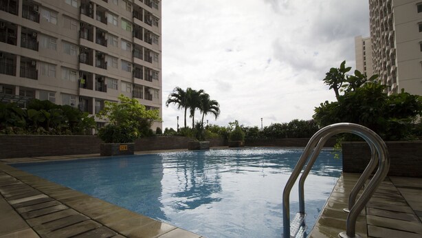 A swimming pool with a metal ladder, surrounded by greenery and tall buildings.