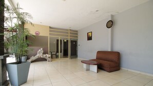 Eine geräumige Lobby mit einer großen Kübelpflanze, einem braunen Sofa und einer Dartscheibe an der Wand.