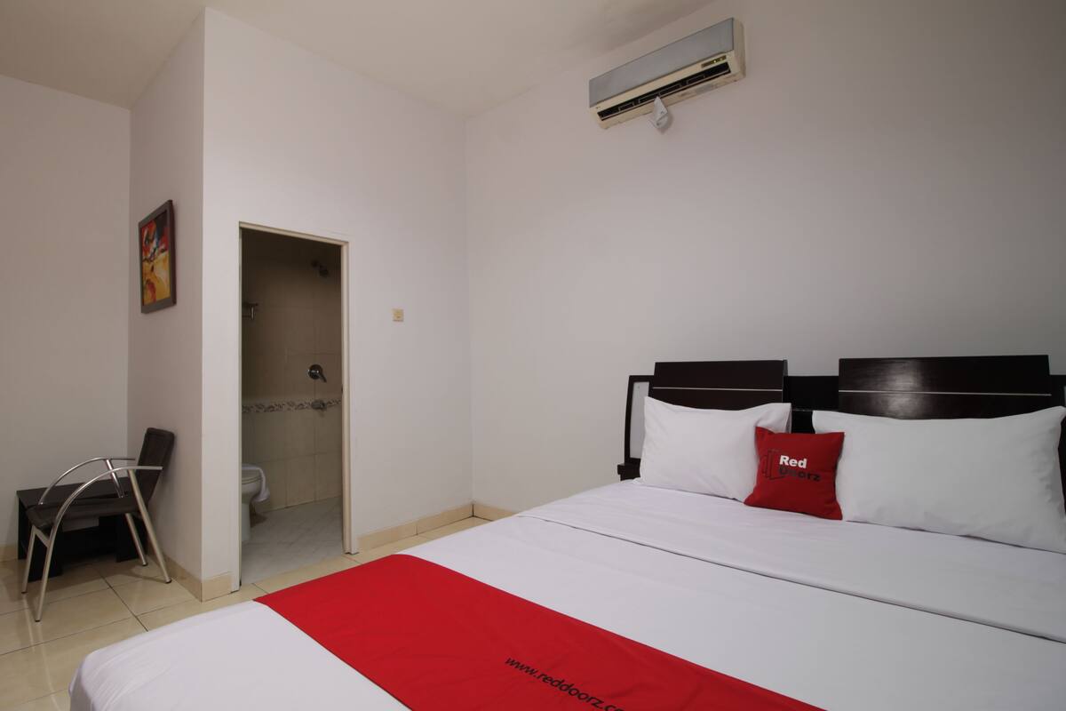 Une chambre d’hôtel avec un lit, une chaise, une porte donnant sur une salle de bain et un appareil de climatisation fixé au mur.