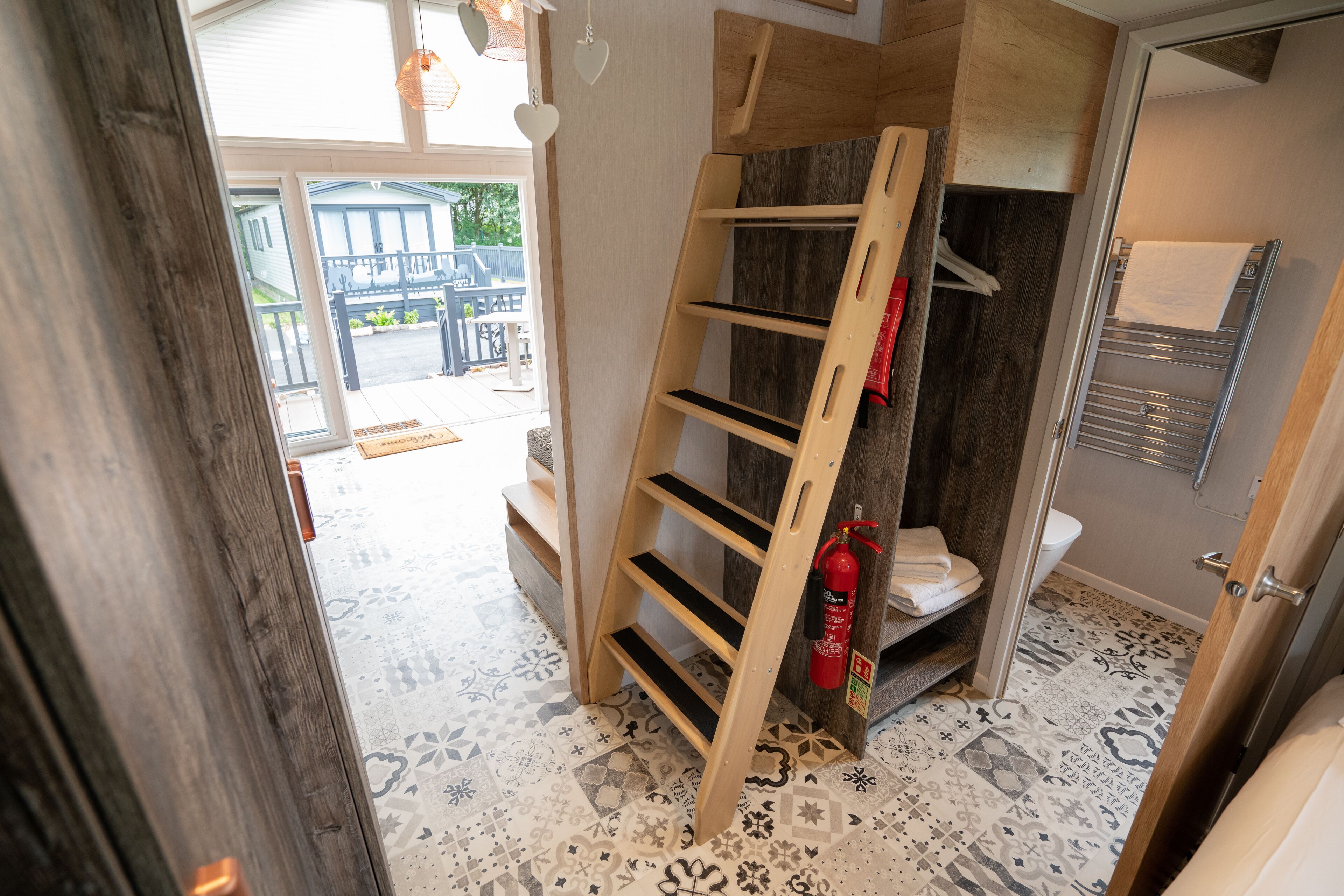 A bathroom with a wooden ladder shelf, a fire extinguisher, and a towel rack.