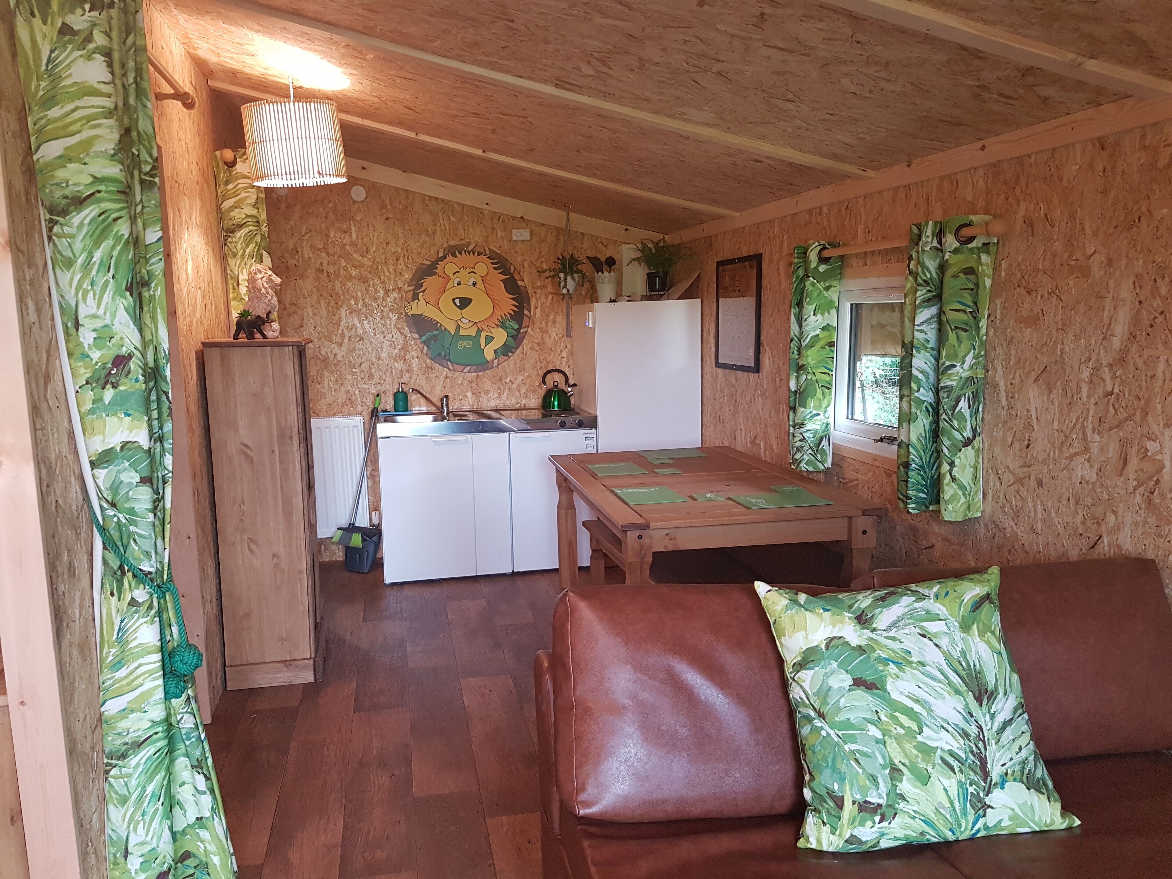 A cozy cabin-style room with a wooden ceiling, a kitchenette, a dining table, and a brown leather sofa.