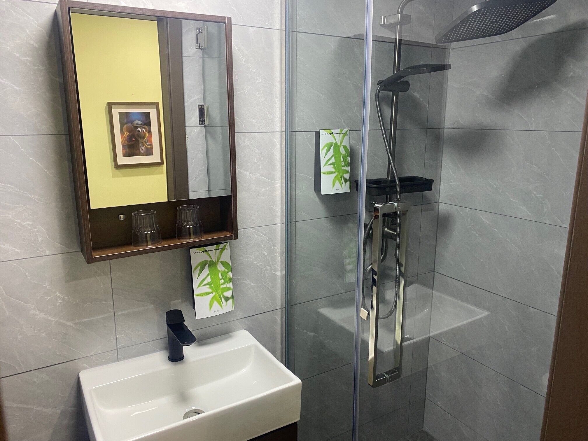 A bathroom with a glass-enclosed shower, a white sink, a mirror, and a shelf with glassware.
