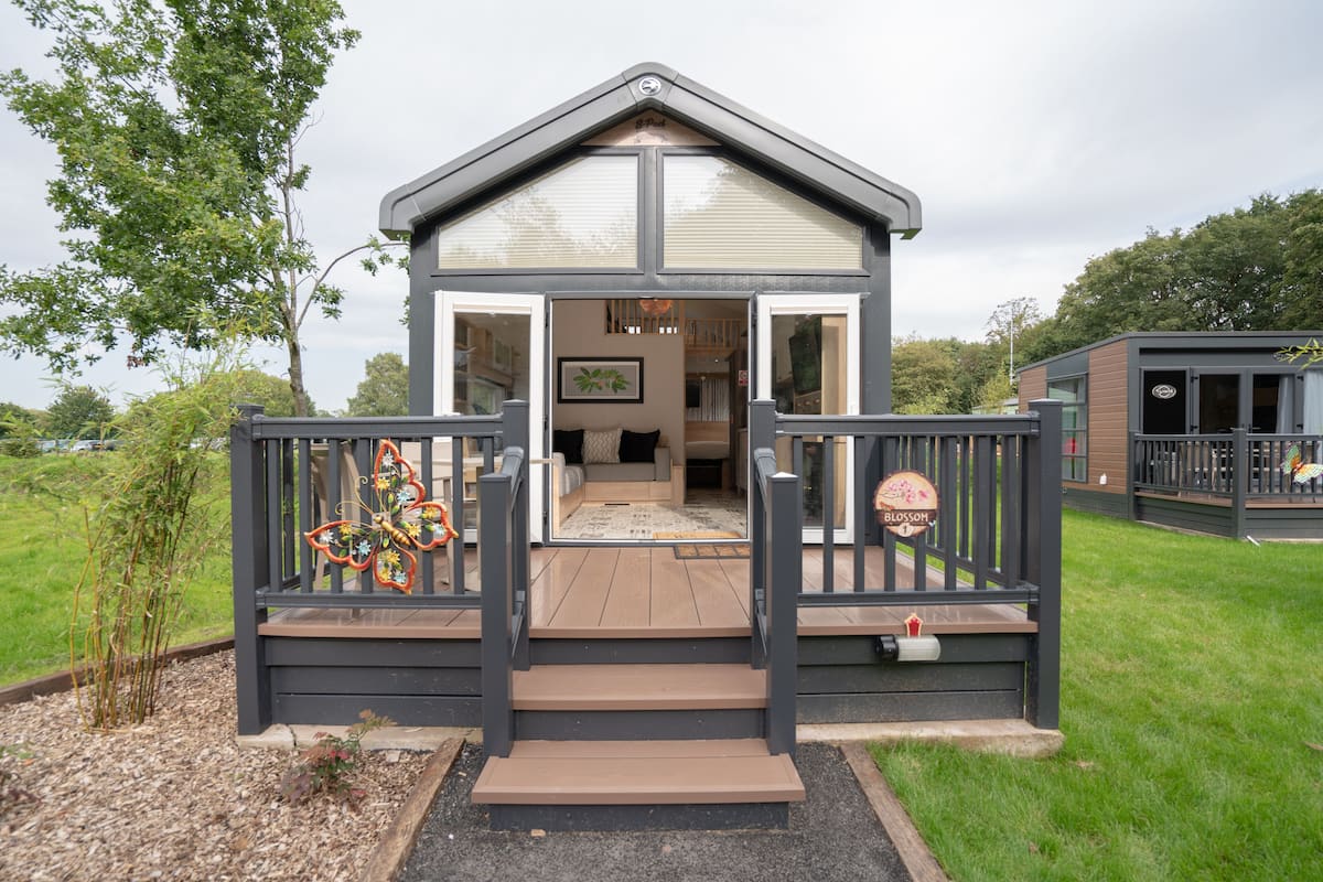 Una casa moderna con terraza de madera, puerta de cristal y un pequeño jardín.