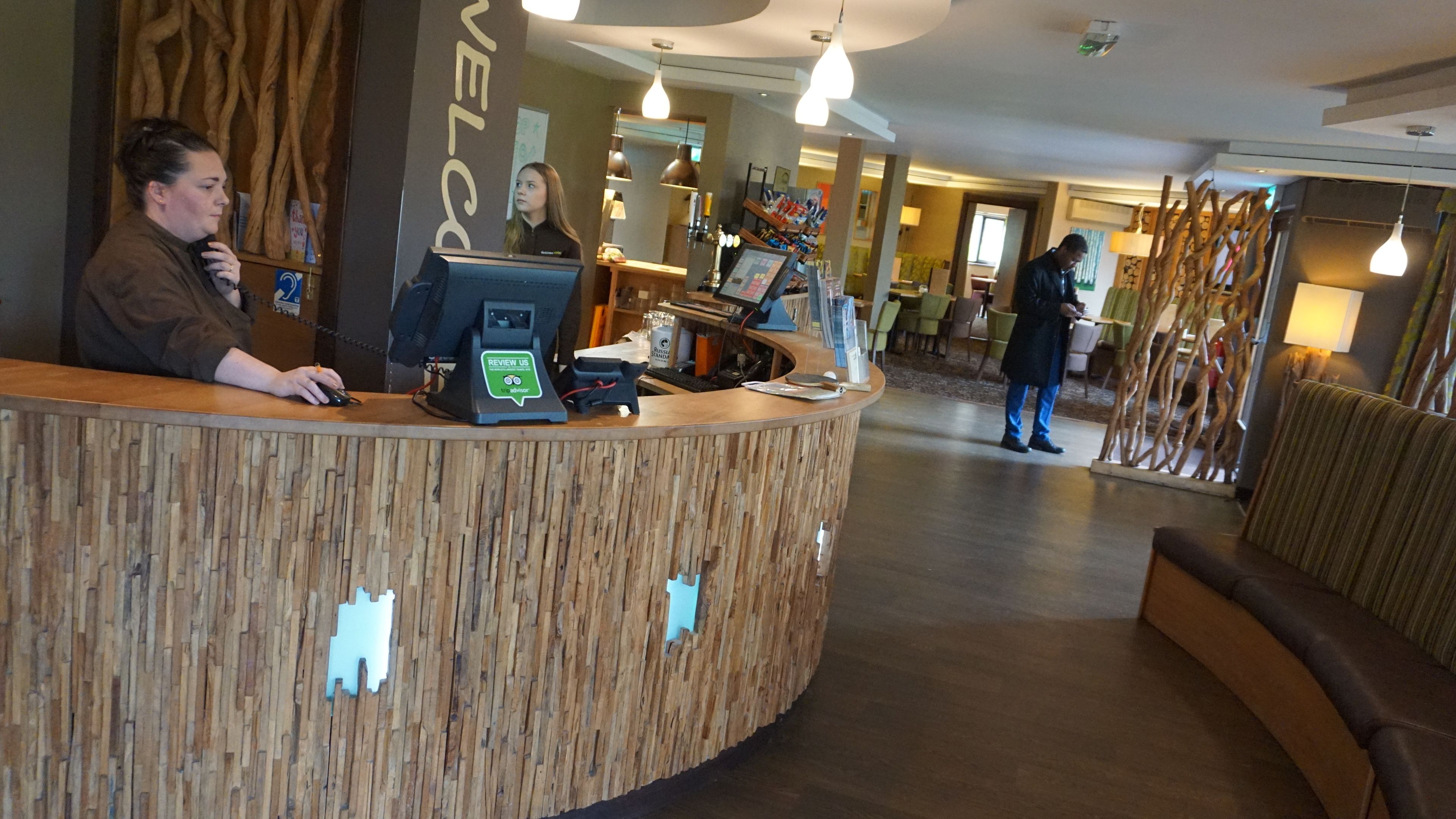Una reception con arredamento in legno, un computer e un cartello con la scritta 'Review Us'. Si vedono sedie e tavoli sullo sfondo.