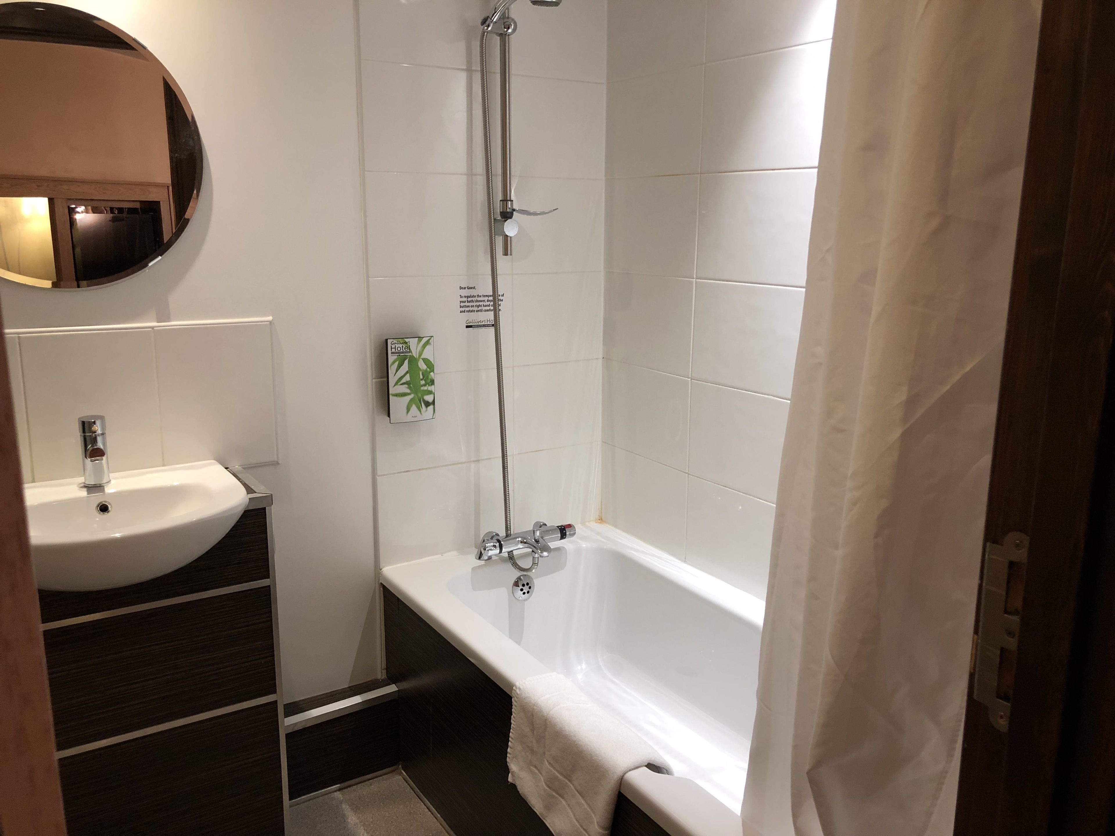 A bathroom with a white sink, a mirror, a shower, and a towel hanging on the wall.