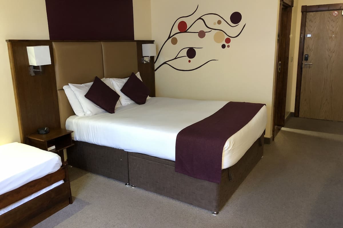 Una habitación de hotel con una cama, una mesita de noche, una lámpara de pared y una puerta.