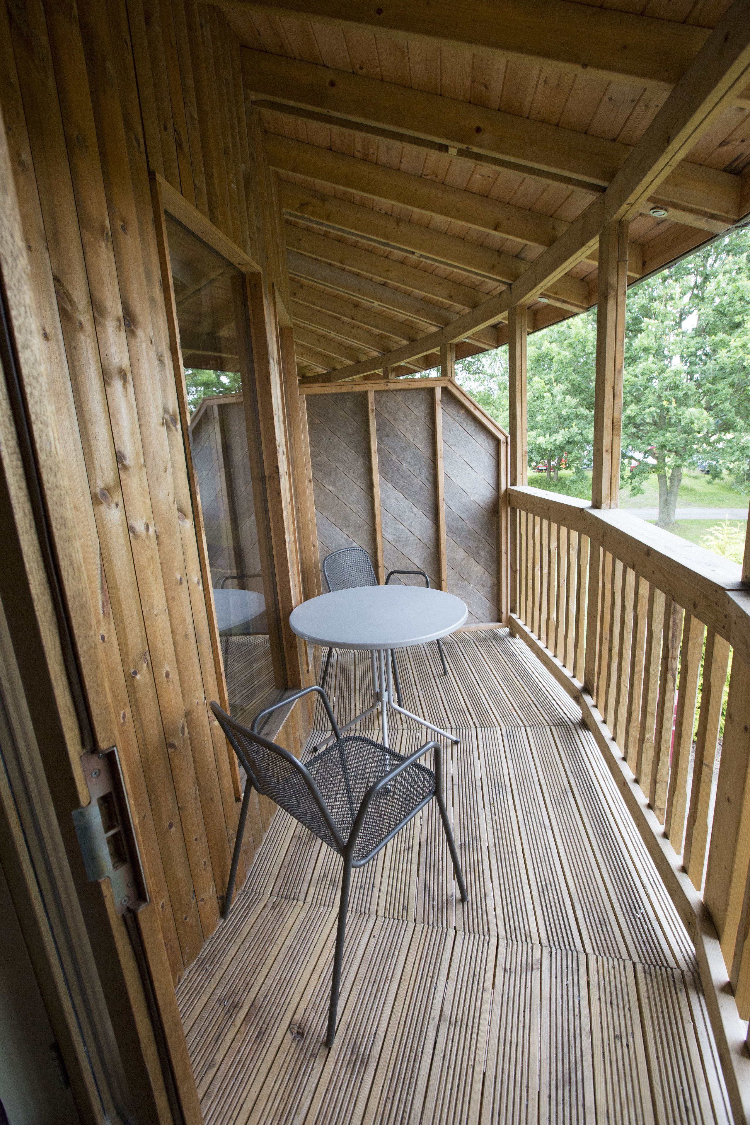 Eine Holzterrasse mit Tisch und Stühlen, umgeben von Holzgeländern und Blick auf Bäume.