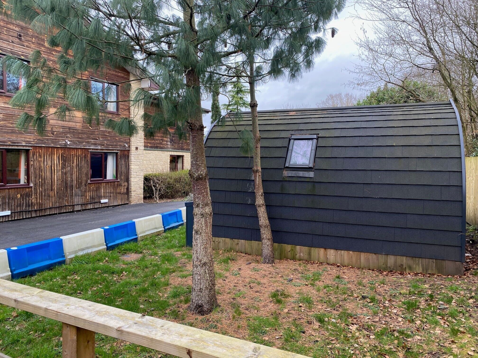 Una casa de madera con un cobertizo pequeño, una cerca azul y blanca y un árbol en el jardín.