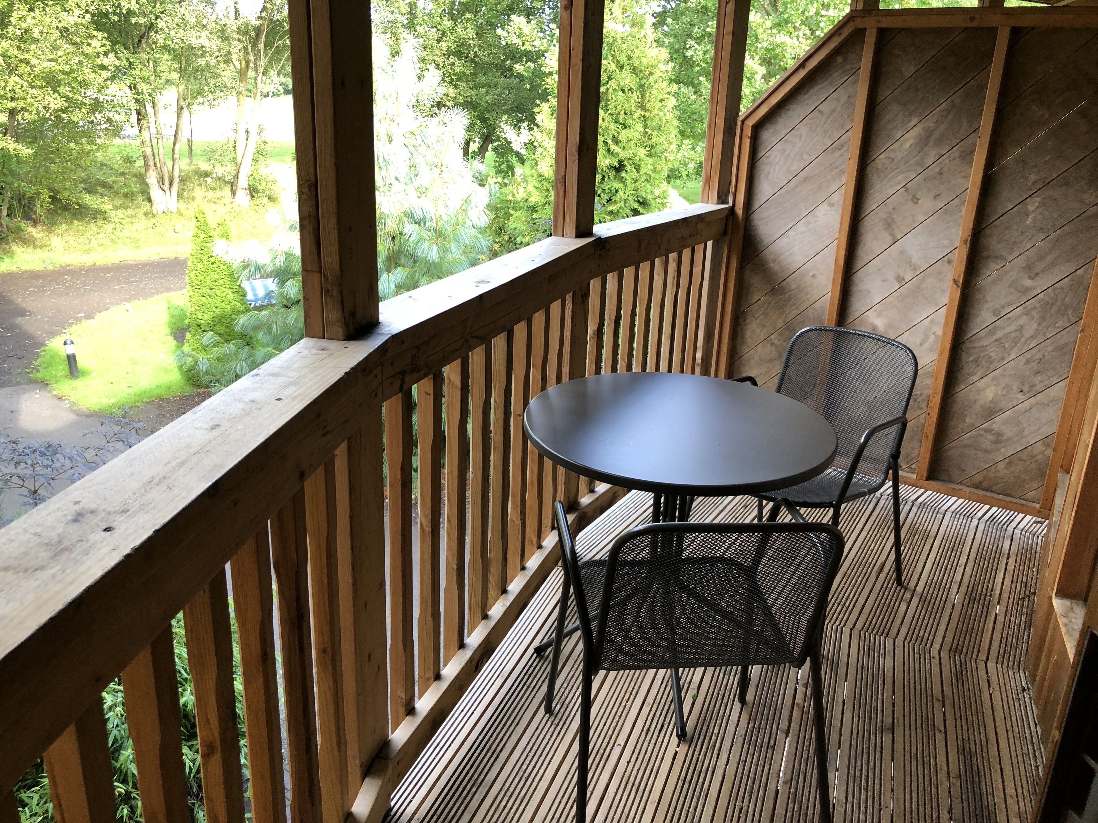 Een houten terras met een tafel en stoelen, uitkijkend op een tuin.