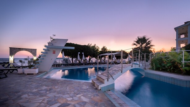 A pool area with stone flooring, lounge chairs, and a decorative archway. - Porto Iliessa by GHH (Zakynthos)