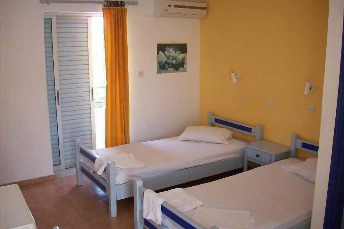 Ett rum med två separata sängar, ett litet sängbord, en luftkonditioneringsanläggning och ett fönster med gardiner.