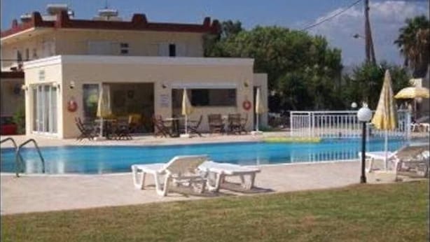 Un hotel amb piscina, gandules i una zona tancada per una tanca.
