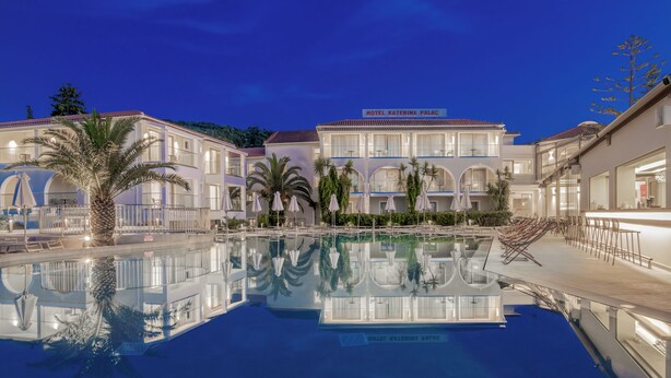 Un hotel con piscina, varios balcones y palmeras.