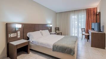 A hotel room with a large bed, bedside tables, a desk with a chair, a television, and a window with curtains.