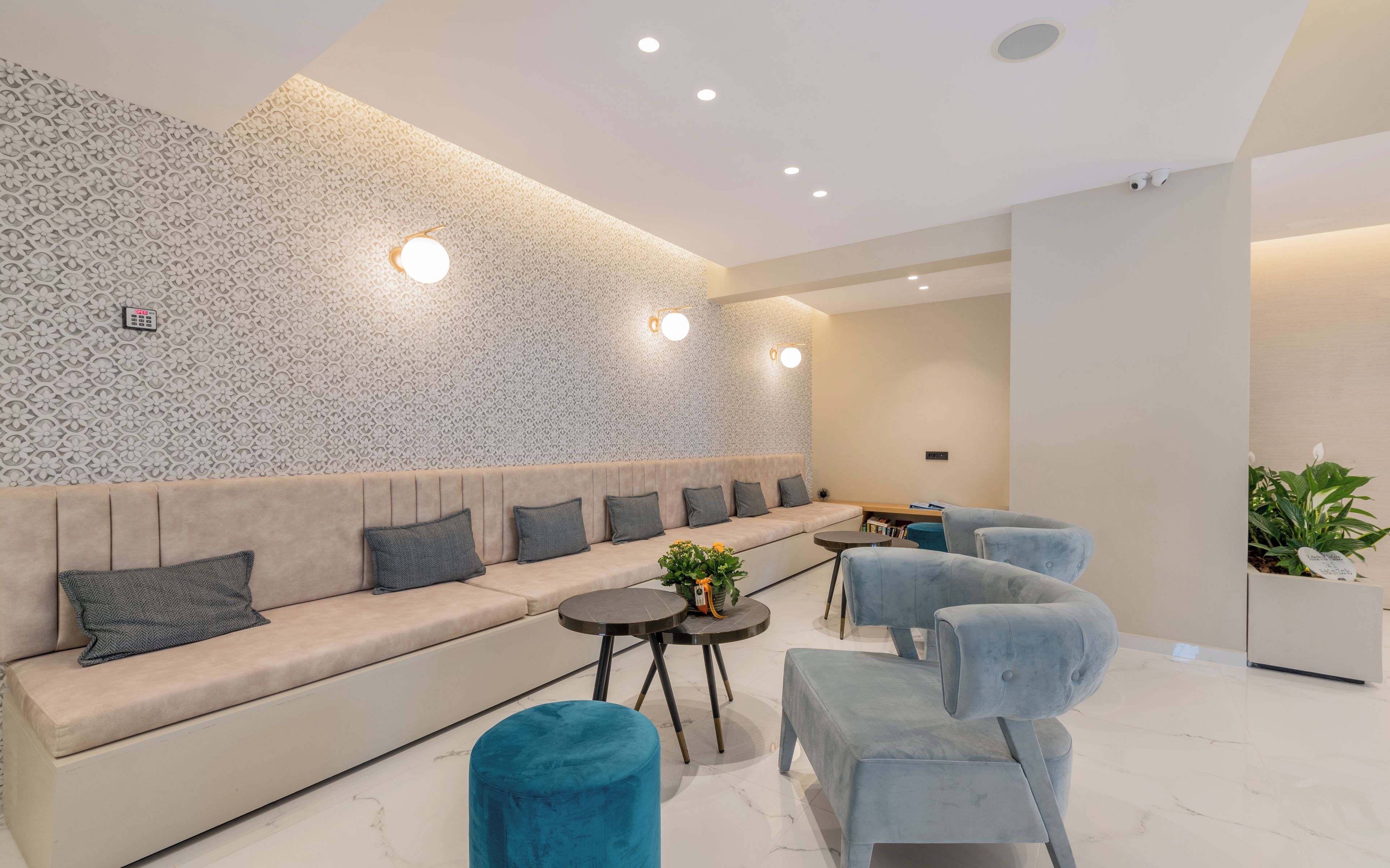 A modern lounge area with a patterned wall, a sofa with cushions, a small table with a plant, and two armchairs.