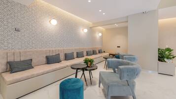 A modern lounge area with a patterned wall, a sofa with cushions, a small table with a plant, and two armchairs.