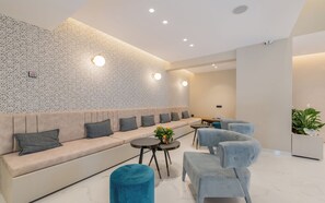 Uma área de estar moderna com parede estampada, um sofá com almofadas, uma mesa pequena com uma planta e duas poltronas.