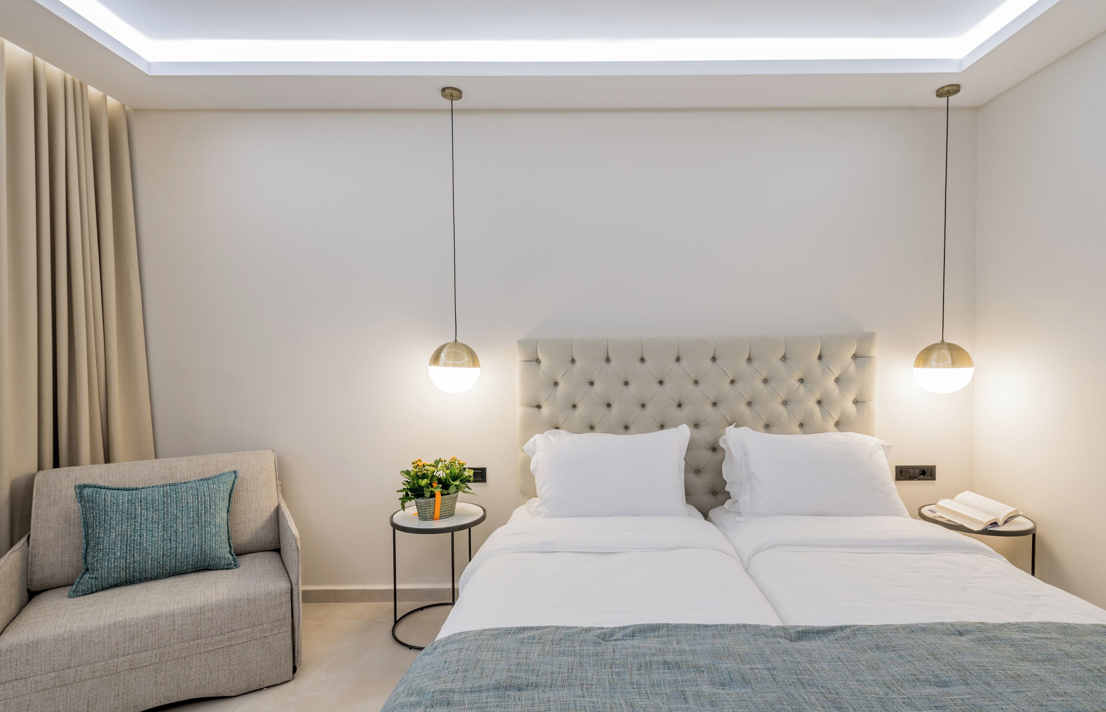 A modern hotel room with a large bed, a sofa, a small side table with a plant, and a bedside table with a phone.
