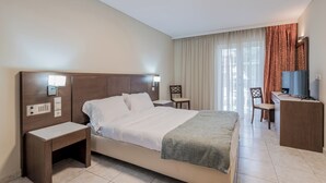 Een hotelkamer met een groot bed, nachtkastjes, een bureau met stoel, een televisie en een raam met gordijnen.