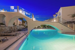 Une piscine dotée d’un pont de verre, de murs en pierre et de chaises longues.