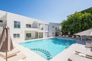 A modern hotel with a swimming pool, lounge chairs, and a covered seating area. - Tarra Seaside Hotel (Apokoronas)