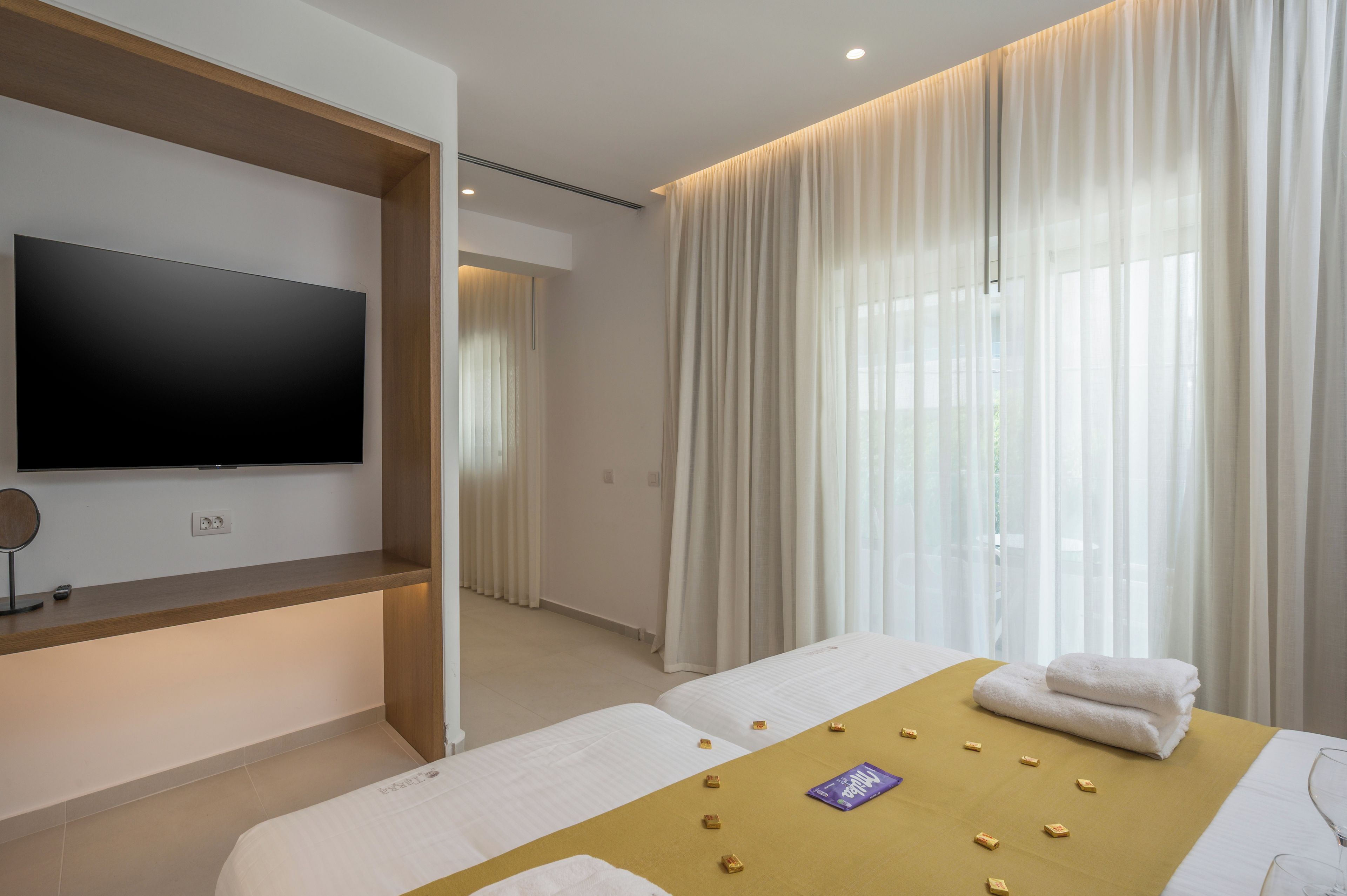 A modern hotel room with a flat-screen TV, a massage table, and a bed with towels.