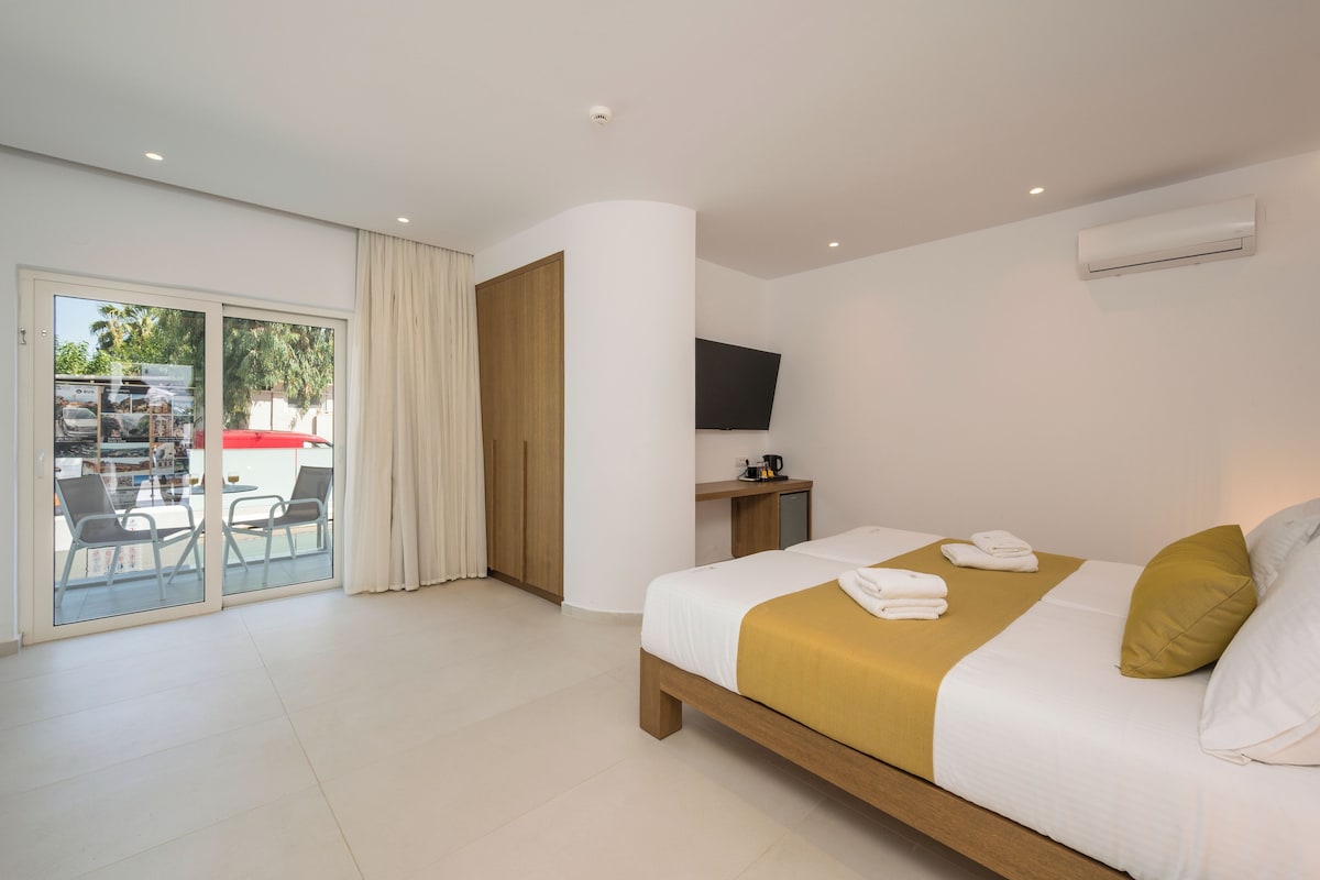 A hotel room with a bed, a TV, a desk, and a sliding glass door leading to an outdoor area.